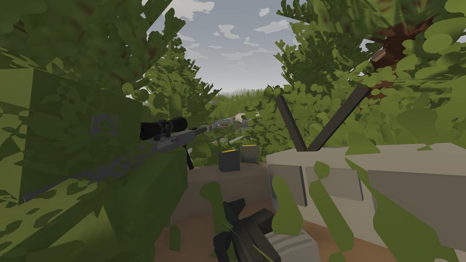 A player lies camoflaged in the grass, watching through the scope of their sniper rifle.